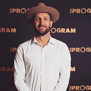 Man with hat looking forward and smiling in front of branded screen